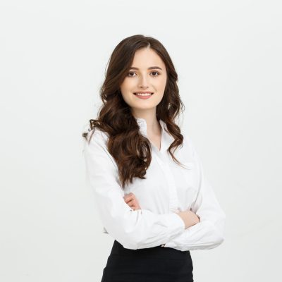Business Concept: Portrait confident young businesswoman keeping arms crossed and looking at camera while standing against grey background.